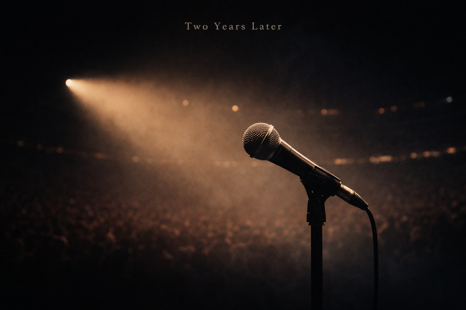 A dimly lit microphone with a blurred crowd in the background, representing reflection on the Kendrick Lamar and Drake rap battle two years later