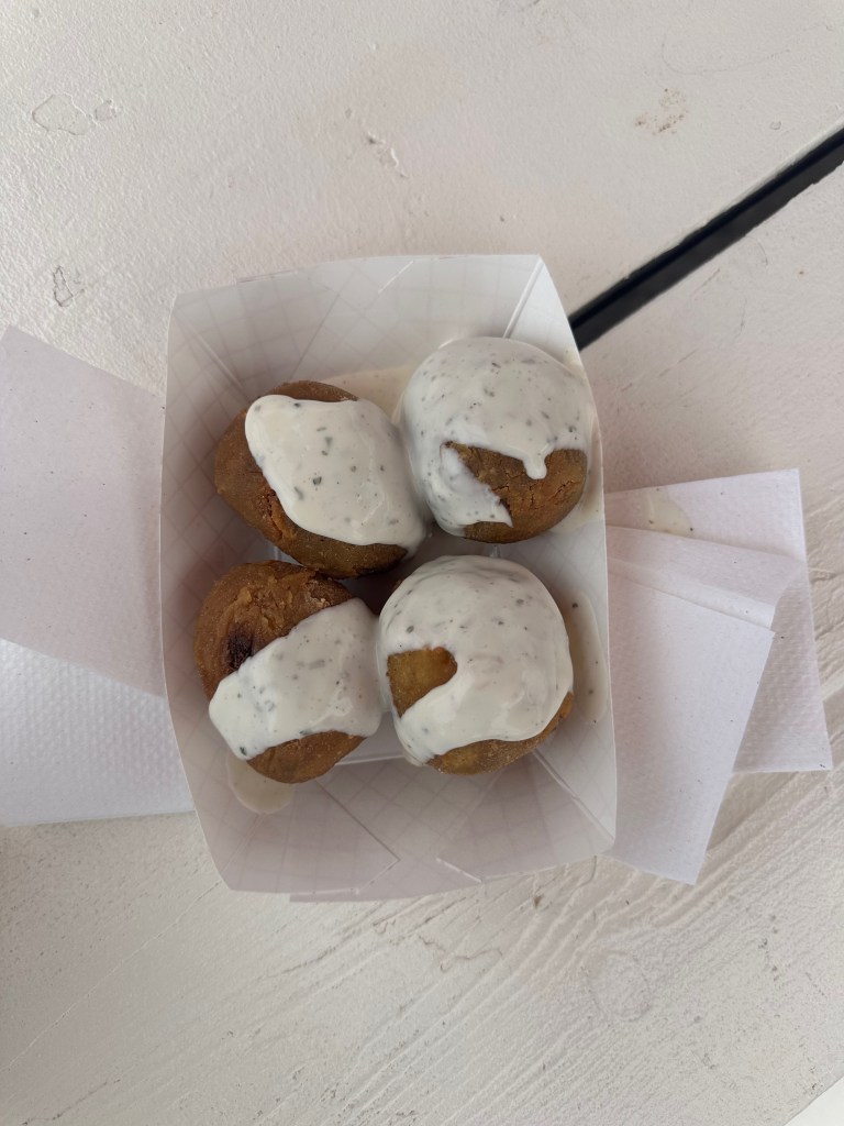 Deep-fried boudin balls topped with ranch in a paper tray.