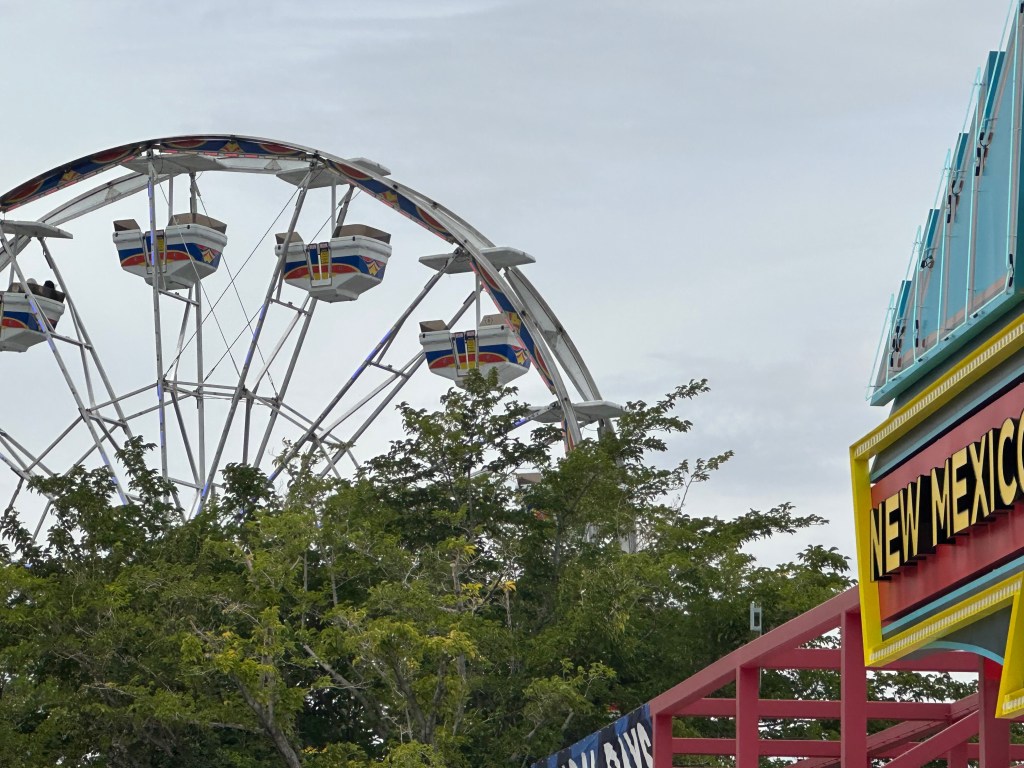 Ferris wheel rising above trees near the New Mexico State Fair entrance.